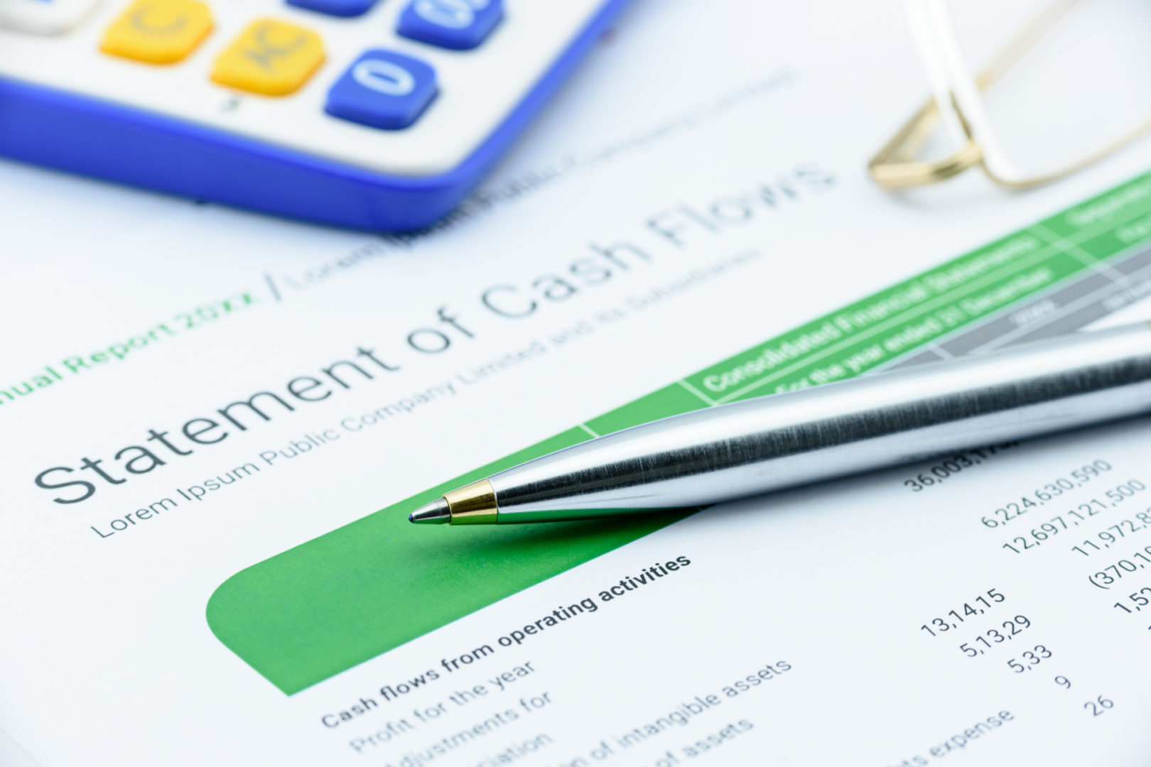 Blue ballpoint pen on a statement of cash flows with eye glasses and a calculator.